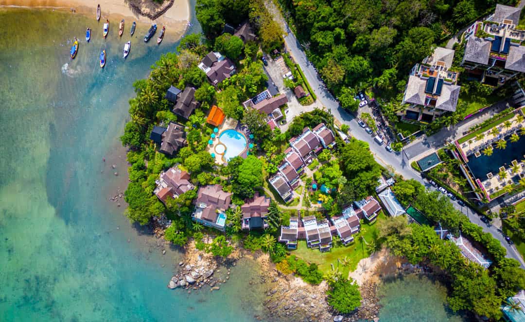 Aerial view of Kamala Beach Estate, with tropical gardens, pools and buildings beside the rocky coast